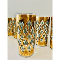 five gold and blue glass cups sitting on a table together, one is filled with flowers