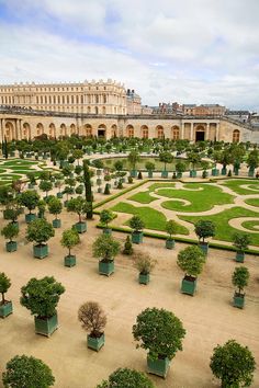 a large garden with many trees and bushes in front of a palace like building on the other side