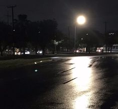 an empty street at night with the lights on and no cars in the road behind it