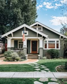 a gray and white house with an american flag on the front door, green grass and trees