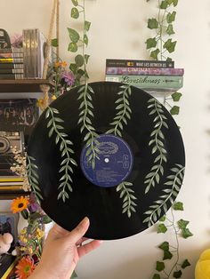 a person holding up a record in front of a wall with plants and books on it