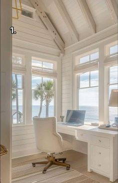 a white desk with a laptop on it in front of two windows overlooking the ocean