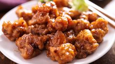 a white plate topped with meat covered in sauce and chopsticks next to a salad