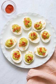 deviled eggs topped with guacamole and tomatoes on a white platter