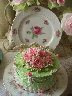 there is a green cake with pink flowers on the top and two plates next to it