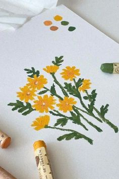 some crayons are laying on top of a piece of paper with flowers painted on it