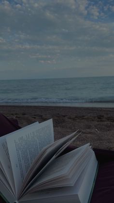 an open book sitting on top of a table next to the ocean under a cloudy blue sky