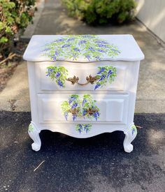 a white dresser with blue and green flowers painted on the drawers is sitting in front of a house