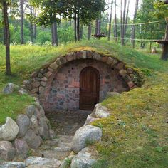 a small house made out of rocks in the middle of a forest with grass on top