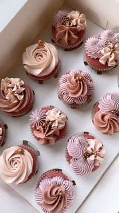 twelve cupcakes with pink frosting in a white box on a table top