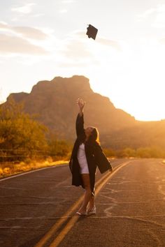 a woman in white shirt and black jacket flying a kite on the side of road