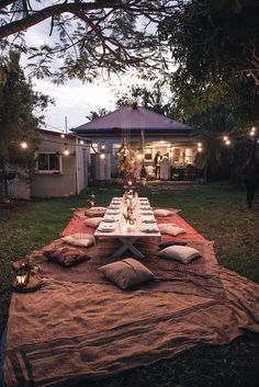 an outdoor table set up for dinner with lights strung from the trees and candles on it