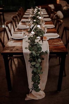 the long table is set with white plates and greenery