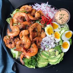 a black plate topped with salad and shrimp next to an egg on top of lettuce