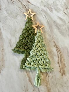 two crocheted christmas trees on a marble surface with gold stars hanging from them