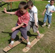 two young boys are playing on wooden skis in the grass with one boy holding his hand out