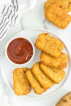 some fried food on a white plate with ketchup and dipping sauce next to it