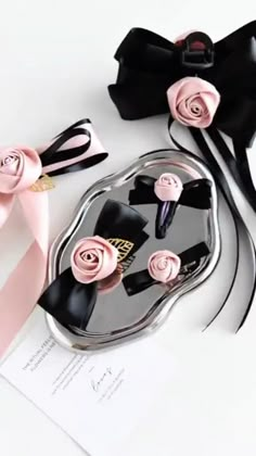 two pieces of black and pink hair accessories on top of a white table with ribbon