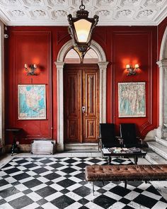 a room with red walls and black and white checkerboard flooring, two chairs in front of the door