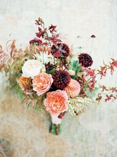 an arrangement of flowers in a vase against a wall with peeling paint on the walls