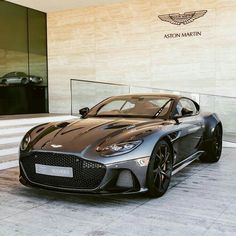 a grey sports car parked in front of a building with the name aston martin on it