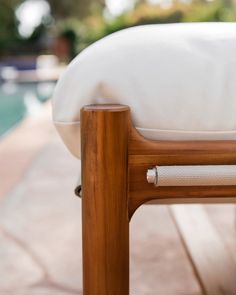 a wooden chair with a white pillow on it's backrest next to a swimming pool