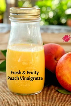 Bottle of fresh peach vinaigrette set on table with two fresh peaches next to it.  Blurred green trees in background.