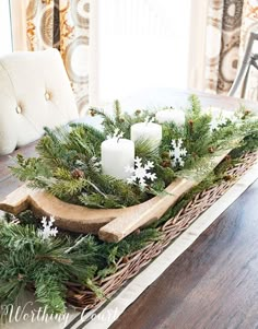 a wooden tray with candles and greenery in it sitting on a table next to a chair