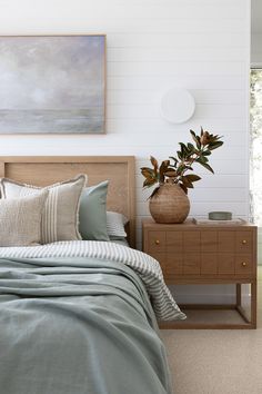 a bed sitting next to a wooden dresser with a plant on it's headboard