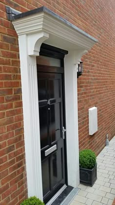 a black front door with two planters on either side and brick building in the background