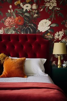 a red headboard in a bedroom with flowers on the wall behind it and a lamp next to it