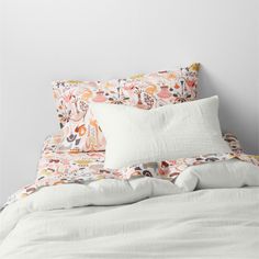 an unmade bed with white linens and colorful floral pillow cases on top of it