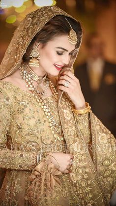 a woman in a bridal outfit with jewelry on her neck and hands to her face