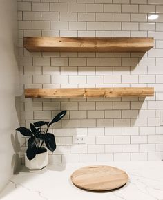 two wooden shelves above a white tiled wall with a potted plant on the counter