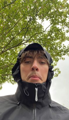 a man wearing a black jacket and hood under a tree