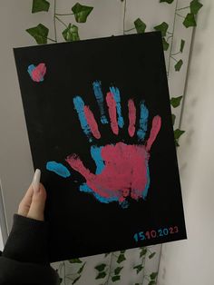 a person holding up a handprint with blue and pink paint on it in front of a wall