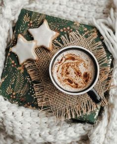 a cup of hot chocolate with cinnamon on top next to two star shaped sugar cookies