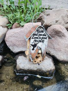 a birdhouse sitting on top of some rocks in the water with a saying above it