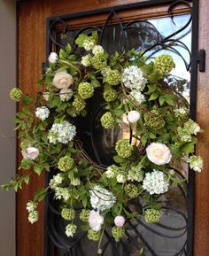 a wreath with white flowers and green leaves hanging on a front door window sill