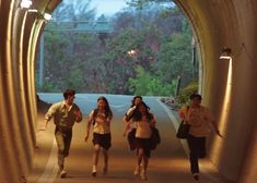 three people are walking through a tunnel with lights on the side and trees in the background