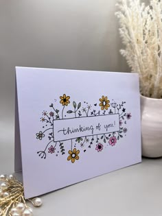 a white card with flowers and the words thinking of you on it next to a potted plant