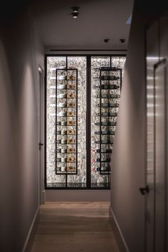 an empty hallway leading to a wine cellar with lots of bottles on the glass doors