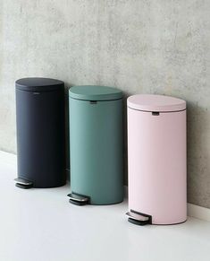 three trash cans are lined up against a wall, one is pink and the other is blue