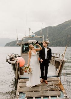 a bride and groom standing on a dock in front of a boat