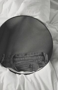 a black and white photo of an empty round mirror on a bed with linens