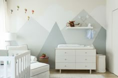 a baby's room with mountains painted on the wall and a crib in the foreground