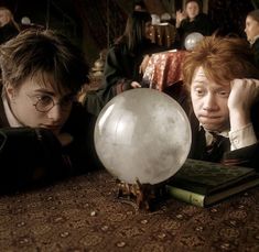 two harry potters look at a crystal ball on a table