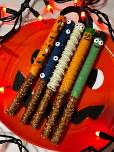 four halloween candy sticks with eyes and noses on an orange plate surrounded by string lights