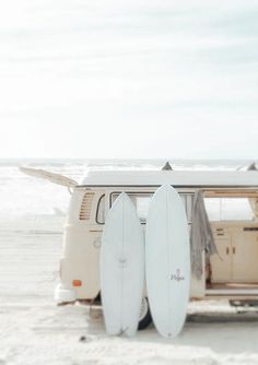 two surfboards are propped up against the back of a camper van at the beach