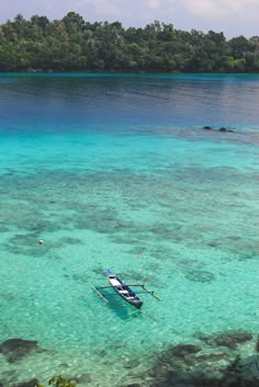 a small boat floating on top of a blue ocean next to a lush green forest